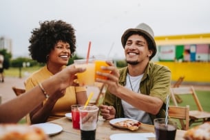 Friends toasting with drink sitting at outdoor table in restaurant