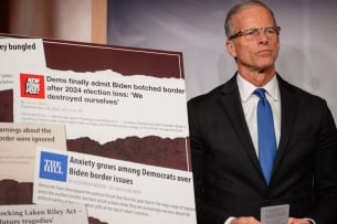 John Thune stands next to a poster of screenshots about the Democrats and border security