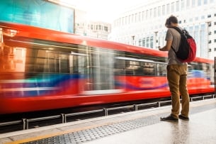 Man with a backpack stands next to an incoming train.