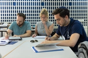 Three rabbinical students sit around a table looking at Jewish texts.