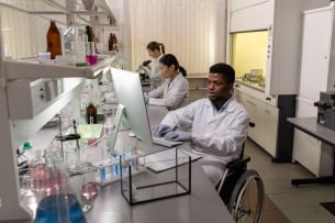 Three young researchers work in a science lab; the researcher in the foreground uses a wheelchair.