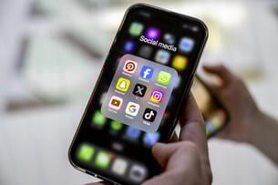 A man holds a mobile phone showing logos of social media applications