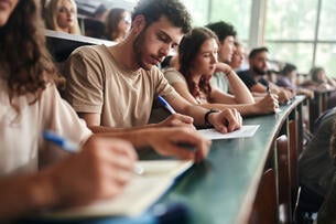 Male university student and his classmates writing an exam during a class in amphitheater.
