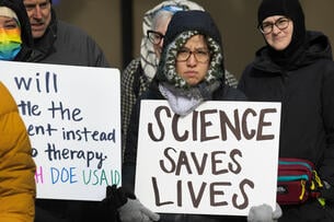A person in a jacket holds a white sign that says "science saves lives" in black text