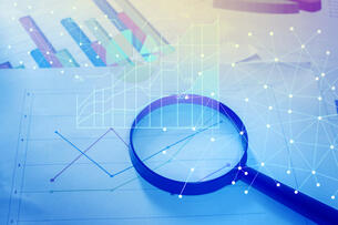 Magnifying glass and documents with analytics data lying on table.