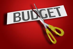 A pair of scissors cuts through a piece of paper with the word "BUDGET," against a red background.