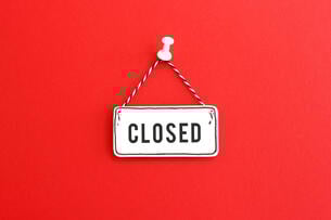 A photo of a handmade "closed" sign, on clapboard, tacked to a red background.