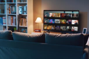 A photo of a relatively dark living room with the landing page for a streaming service visible on the TV, which sits next to a bookcase.