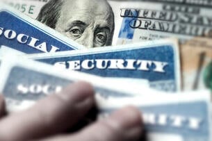 A photo of a stack of Social Security cards atop a $100 bill.