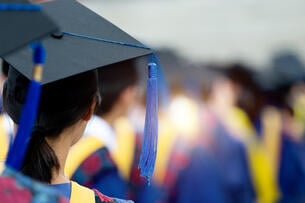 A rear view of graduates during commencement wearing blue and yellow regalia and graduation caps.