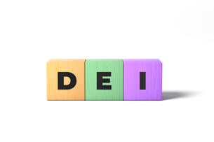 Three wooden alphabet blocks of different colors spell the acronym "DEI."