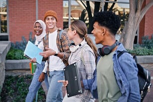 Four students walk to class on a college campus outside
