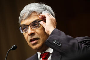 Dr. Jayanta Bhattacharya, a man with silver hair and glasses wearing a suit and red tie