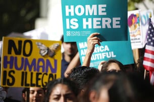Students hold signs that read "no human is illegal" and "home is here."