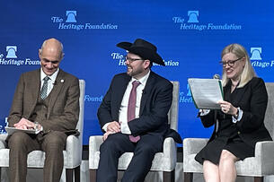 A photo of three panelists speaking at the Heritage Foundation. The man in the center is wearing a cowboy hat.