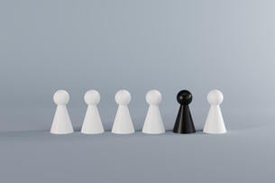 A row of six pawns (chess pieces) against a gray background. Five of the pawns are white and one pawn, placed second to the right, is black.