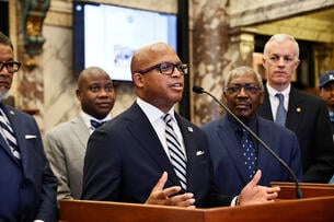 Former Jackson State University president Marcus Thompson speaks into a microphone at a podium with other JSU representatives behind him.