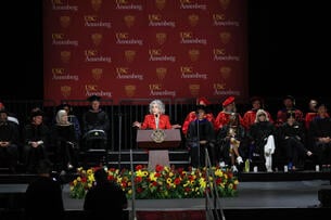 Jane Fonda stands in a red suit in front of a large backdrop displaying USC Annenberg's logo.