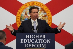 Florida governor Ron DeSantis standing in front of a Florida flag and behind a podium with a sign that says "Higher education reform"