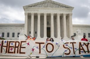 A group of students hold a sign reading "here to stay" in front of the U.S. Supreme Court in Washington, D.C.