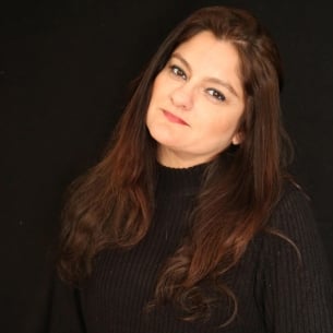 Mehnaz Afridi, a light-skinned woman with long brown hair, wearing a black shirt against a black background