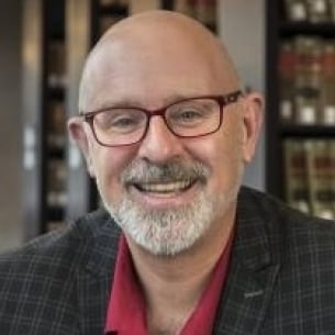 Tom Ginsburg, a light-skinned man with a bald head and a gray goatee and mustache, wearing glasses and a checked jacket and red polo