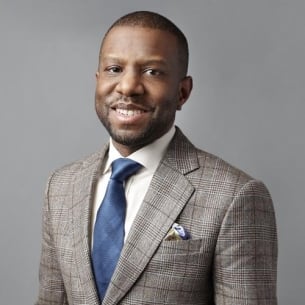 Ivory Toldson, a brown-skinned man with very short dark hair and a mustache and beard, wearing a gray checked suit and a blue tie