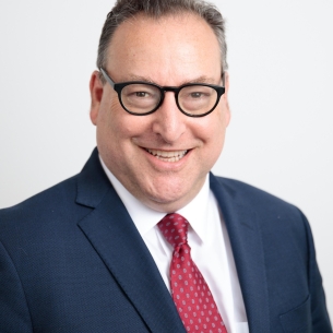 Ken Marcus, a light-skinned man with short dark hair, wearing glasses and a blue suit and red tie