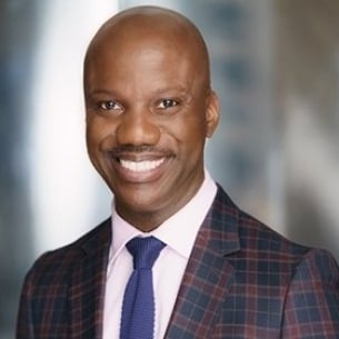 Shaun Harper, a brown-skinned man with a bald head and a mustache, wearing a blue and burgundy plaid jacket with a blue tie.