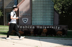 A student wearing a kippah walks in front of a sign that reads "Yeshiva University."