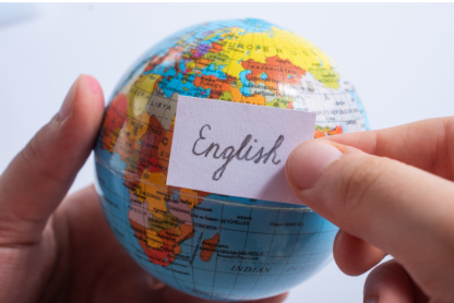 A close-up of a person's hands holding a globe along with a scrap of paper that says, in cursive, "English."