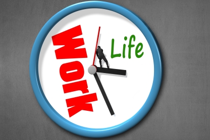 Clock with "Work" written in red taking up more than half of the face of the clock and "life" in green taking up about a fourth, while a man stands on the hands at 3:30 trying to push back the work section