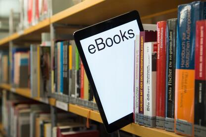 A tablet with the word "ebooks" peeks out from a library shelf lined with physical books.