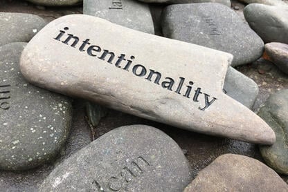 A photo of a pile of smooth stones, with the stone on top bearing the word “intentionality.”