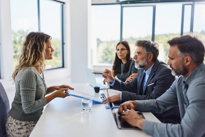 A female job candidate sits across from a group of three people in a job interview. 