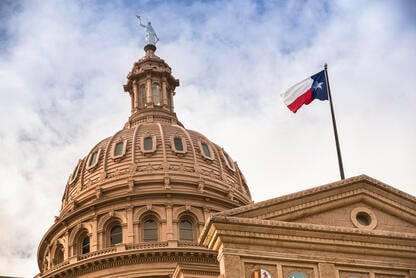 The dome of the Texas capitol, with the Texas state flag flying in front.