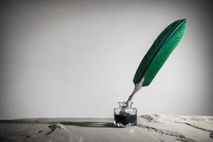 A quill pen in an ink pot against a gray background. 