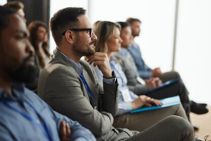 A row of five audience members participating in a seminar of sorts; all appear engaged by the content.
