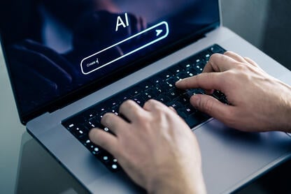 A close-up of hands typing on a laptop with the screen open to an AI chat bot.