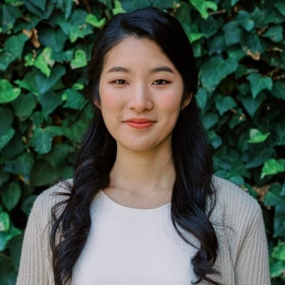 Mina Lee, a woman with light skin and long black hair, wearing a light-colored top and pink lipstick