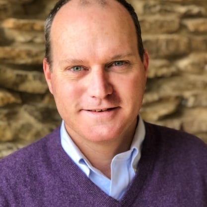 Stephen Monroe, a light-skinned man with dark hair wearing a purple sweater over a blue collared shirt