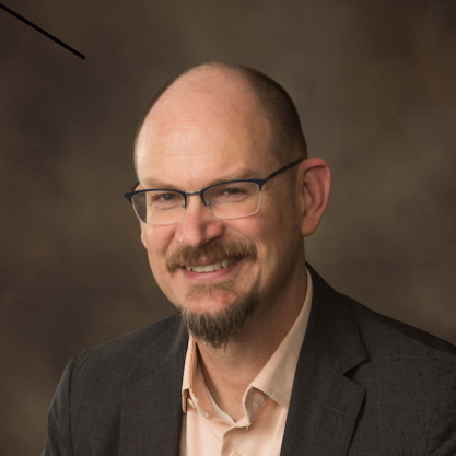 Ted Underwood , a light-skinned man with a brown mustache and goatee, wearing glasses and a suit jacket over an open-collared button-down shirt