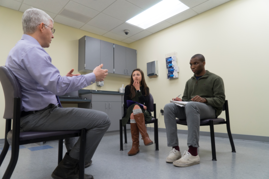 A professor sits with two students in a medical examiner room. 