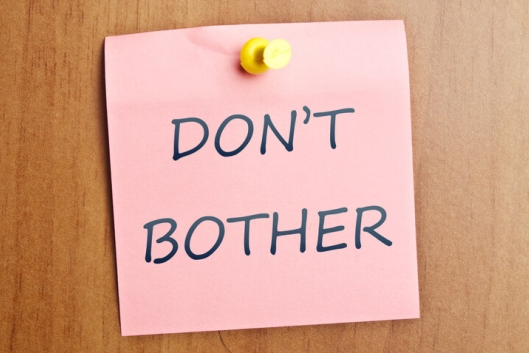 The words "Don't bother" written on a pink note tacked to a wooden door. 