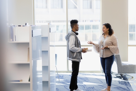 A student speaks with a professor holding a stack of books