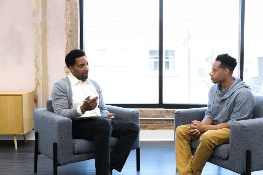 A male counselor speaks with a young male client.