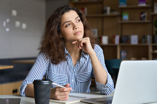 Student looking thoughtful while sitting at a desk with paper and pencil and a laptop on the desk.