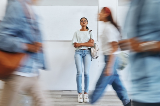 A young woman stands by herself while other people rush by her.