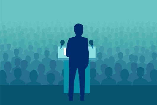 Man standing at podium in front of a crowd of heads without faces fading into background
