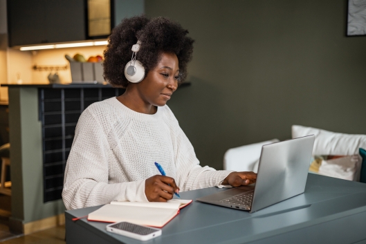 Young African American woman watching online course and writing notes